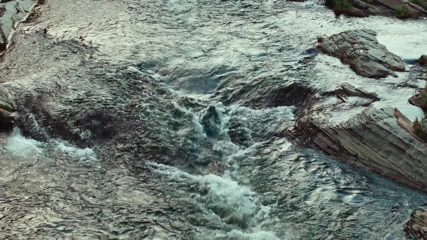 A fast flowing river cuts through gray sedimentary rock