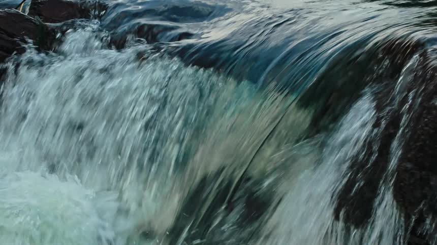The water in a small waterfall cascades over dark mossy rocks