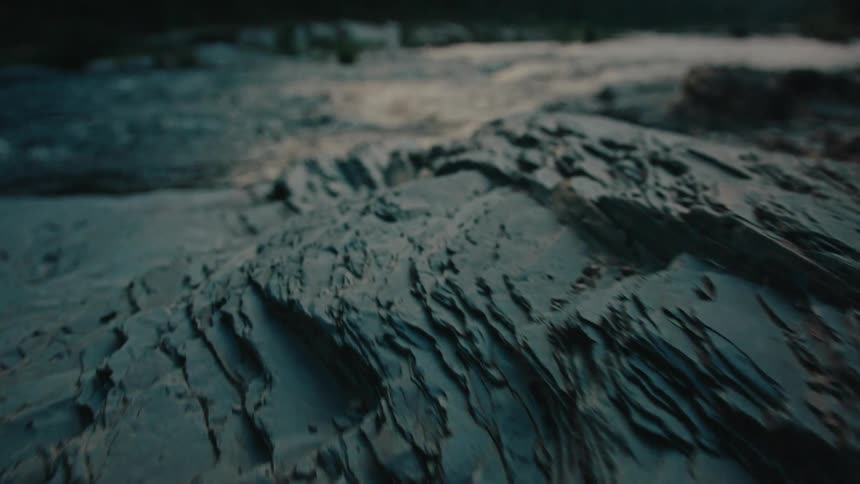 Feet of a person in boots passing over rocks at the edge of a river