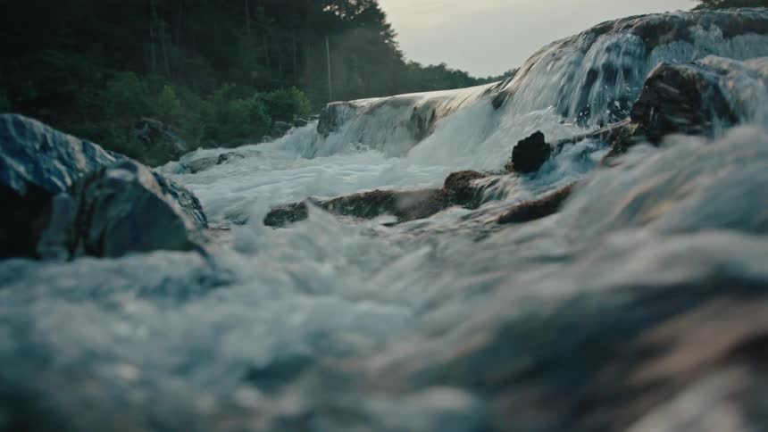 A river with fast water passing between several stones that are on the surface