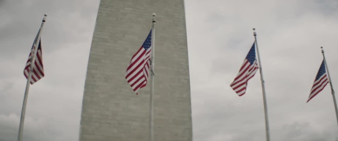 Several united states flags moving in the wind and behind there is a large tall building