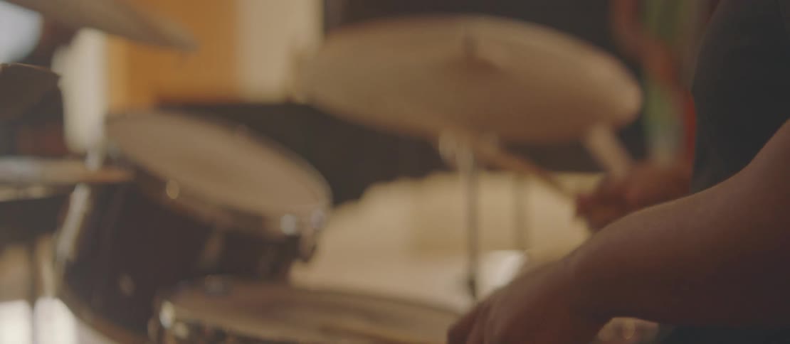 A seated man is holding drumsticks and beating on a small drum of a drum kit