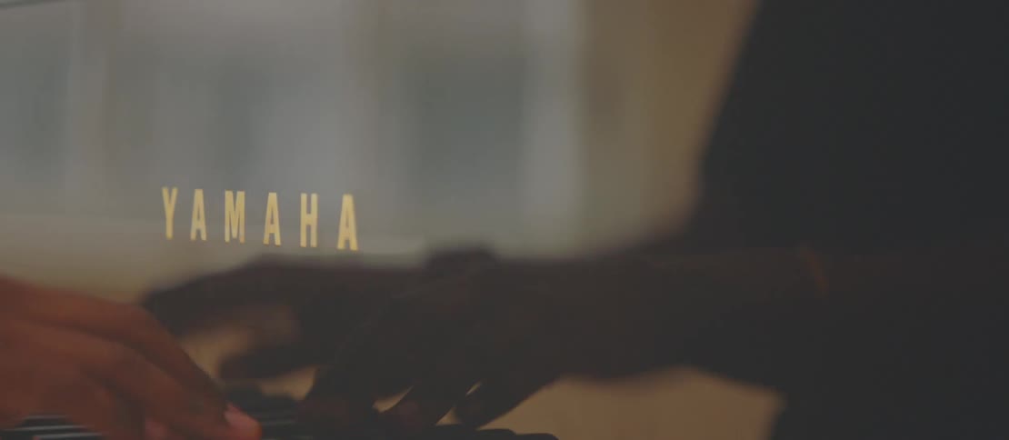 A persons hands playing the keys of a black piano and the person is wearing a gold bracelet