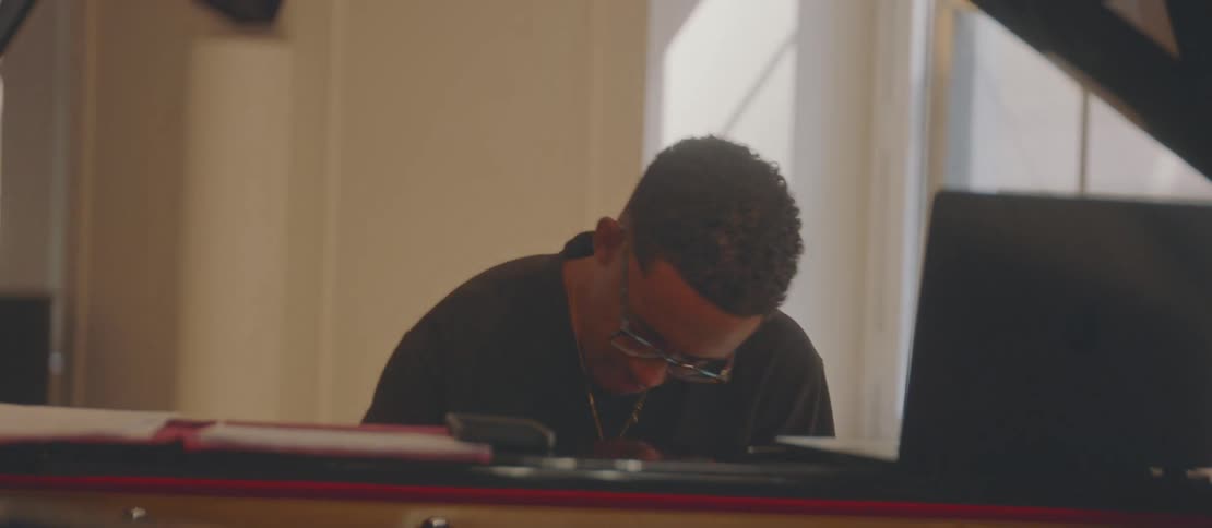 A man is sitting playing the piano and in front of him is an open laptop