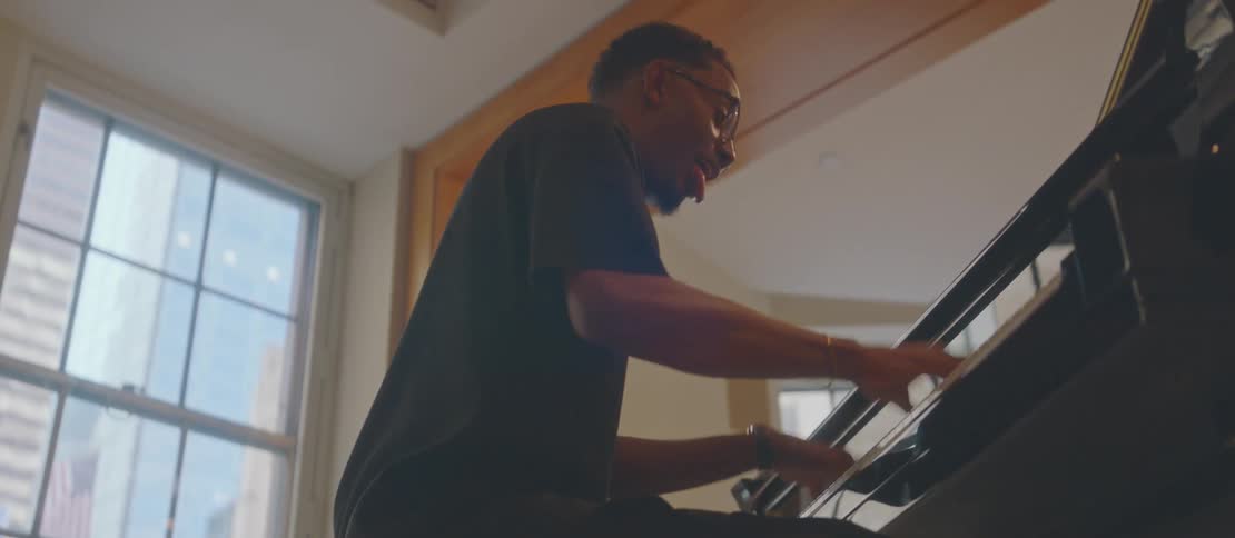 A young man is sitting playing a piano and he is smiling