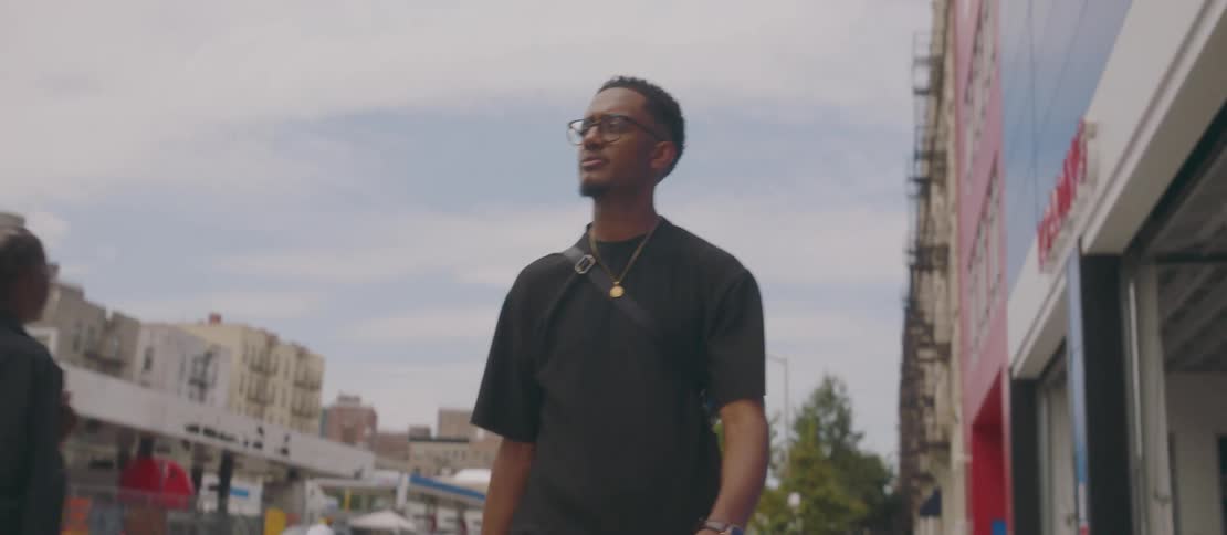 A young man wearing a black tshirt walking on a city street
