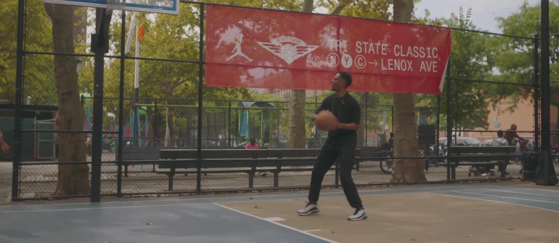 Two black males play basketball at a city park