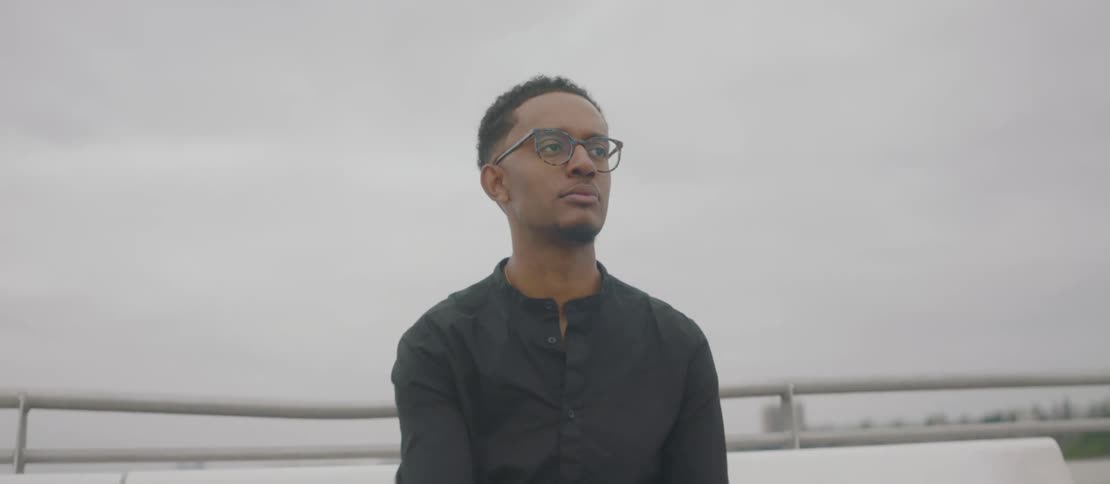 A man sitting by the water adjusts his glasses