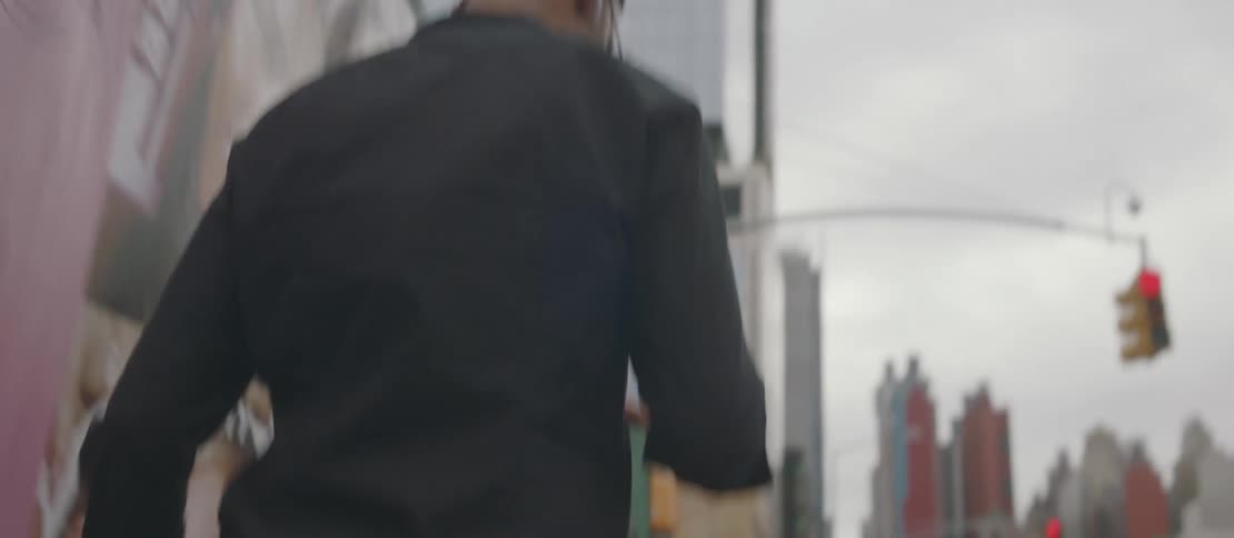A man is holding a black bag and he is walking on a sidewalk and he is wearing glasses and earbuds