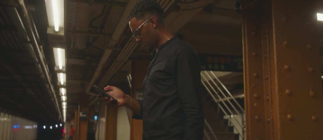 A young man looking at his smart phone while waiting for a train in a subway station