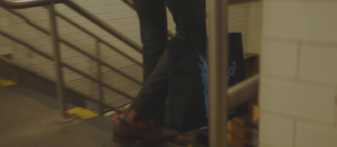 Person descending a staircase in a subway station carrying a black bag and a blue bag