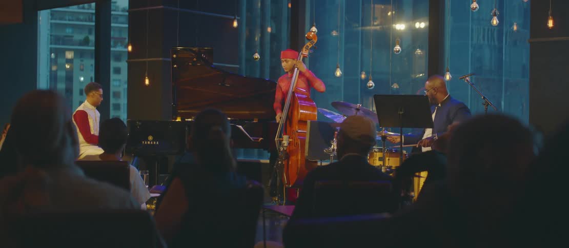 A three piece band plays for an audience in a city venue