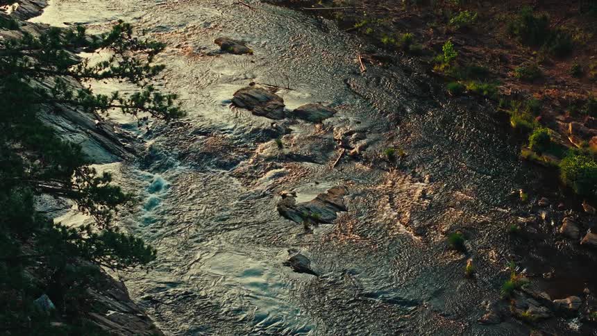 River water churns while passing over the boulders between a sloping stone bank and a field