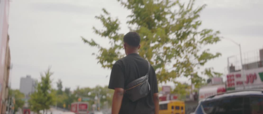 A young man walks along the sidewalk passing by stores and shops on the city street