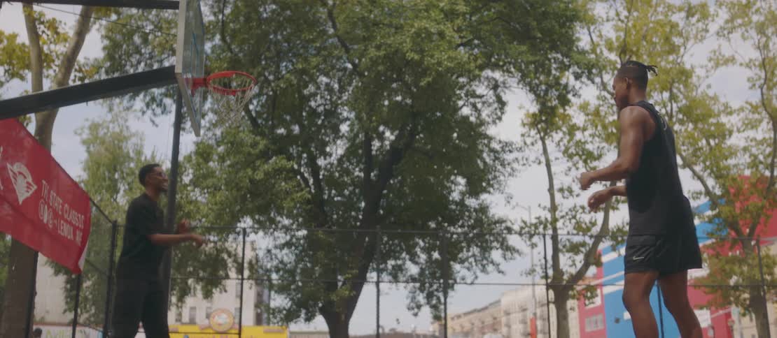 Two black males have fun shooting hoops at a city park