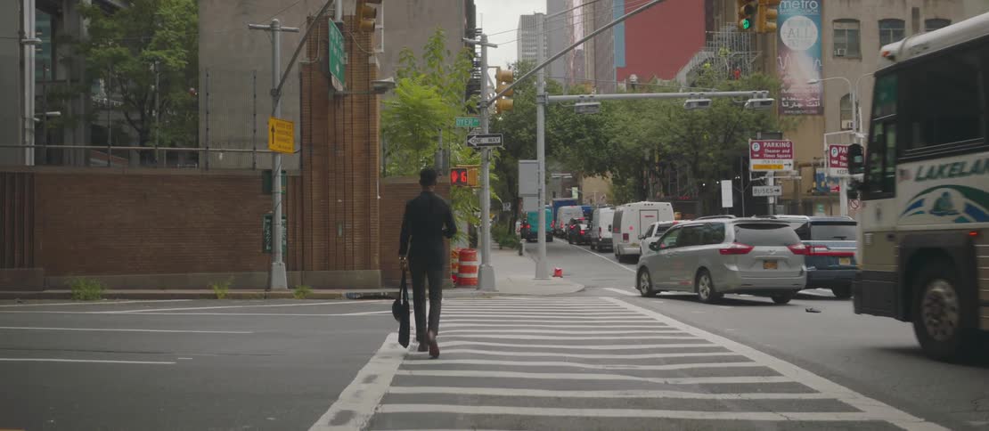 A man with his back turned is crossing a street using a pedestrian crossing and on the right side there are several cars on a street with a lot of traffic