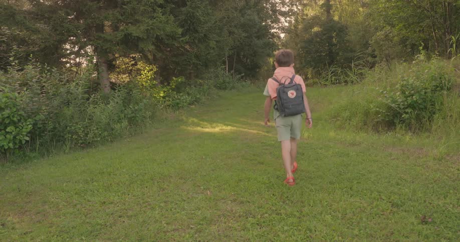Boy walks along a grassy path surrounded by trees and bushes