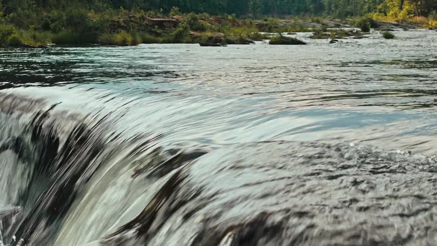 Closeup of a small waterfall with rapidly flowing water surrounded by dense greenery in the mountains