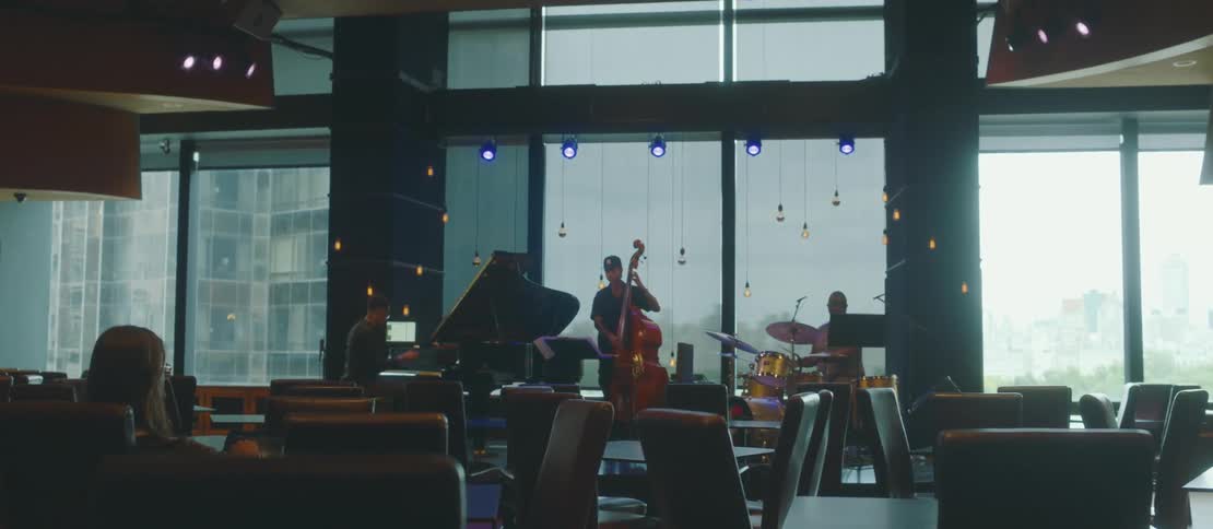 Jazz trio consisting of a pianist a double bassist and a drummer playing in an elegant indoor setting with large windows in the background