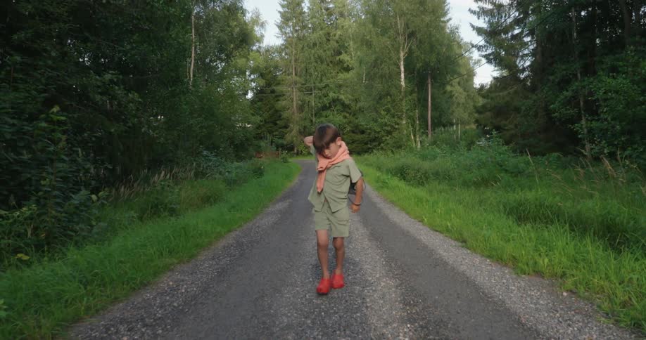A child walking on a dirt road adjusting a backpack on his back while walking