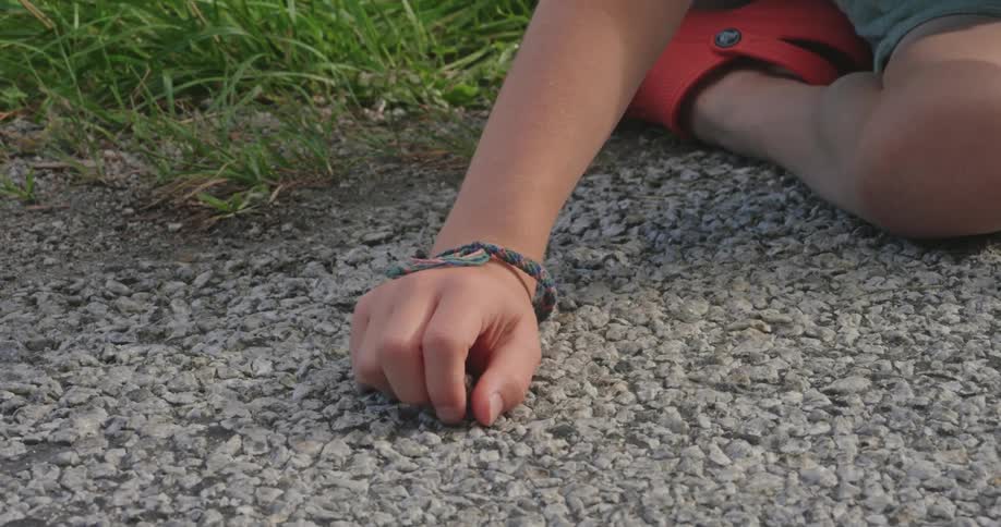 Little boy sitting on the ground with stones catching an insect with his hand