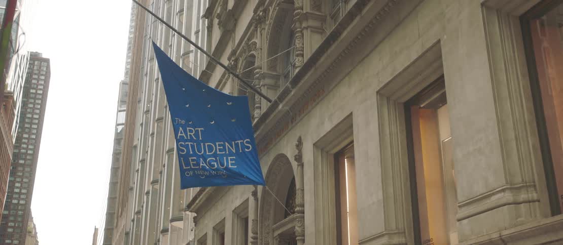A classical building in a city with a banner hanging from the entrance and people passing in front of it