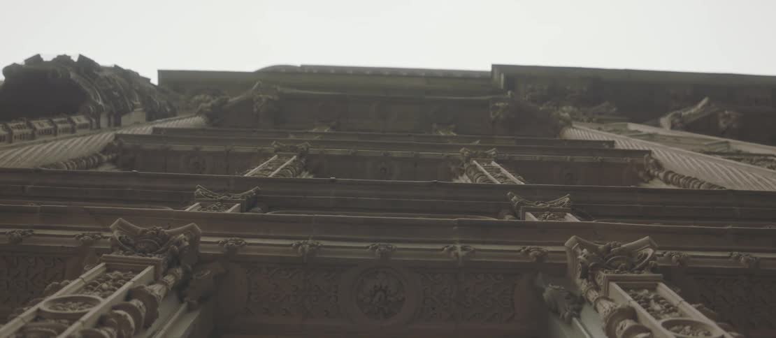 An upward view of a tall ornate building with intricate architectural details including elaborate carvings and decorative columns all framed against a pale sky emphasizing the buildings grandeur and historical design