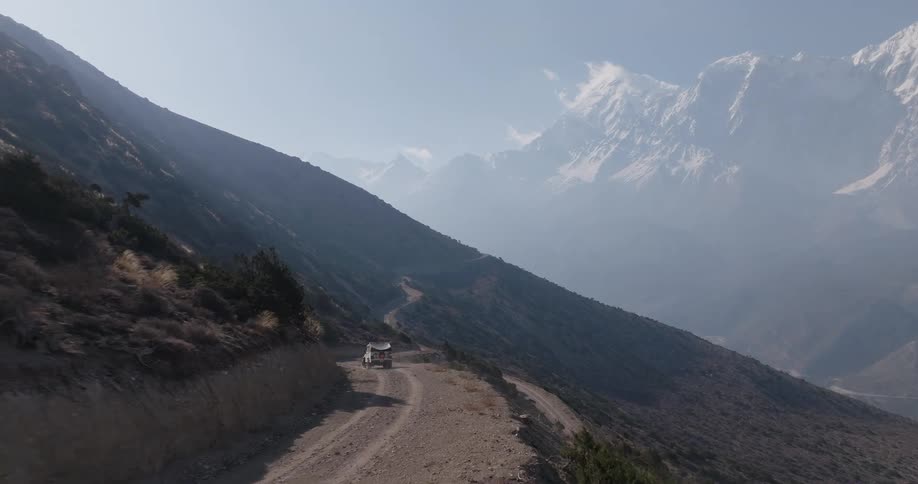 White jeep traveling on a dirt road in a mountain with undergrowth and snowy mountains on the horizon