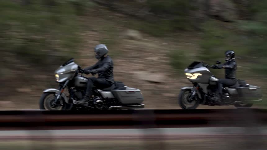 Two motorcycles traveling along a paved road surrounded by vegetation