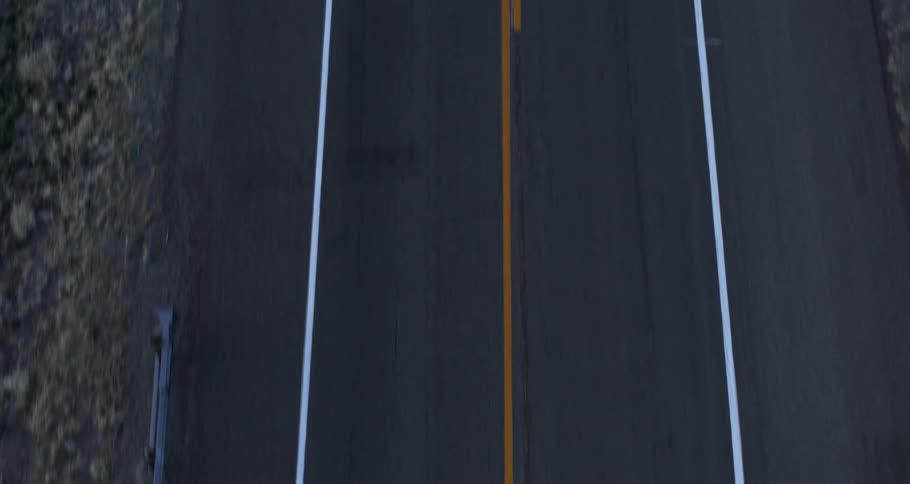 An aerial view of two motorcycles driving on a road with a yellow line in the center