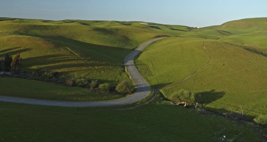 A narrow path sits between hills covered in grass with the sun shining
