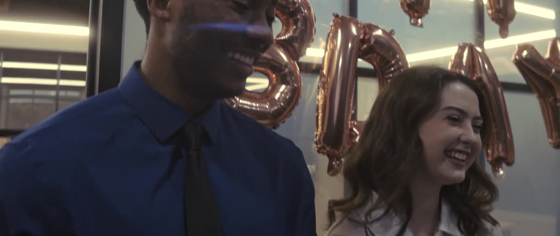 Man and woman side by side with happy birthday balloons in the background