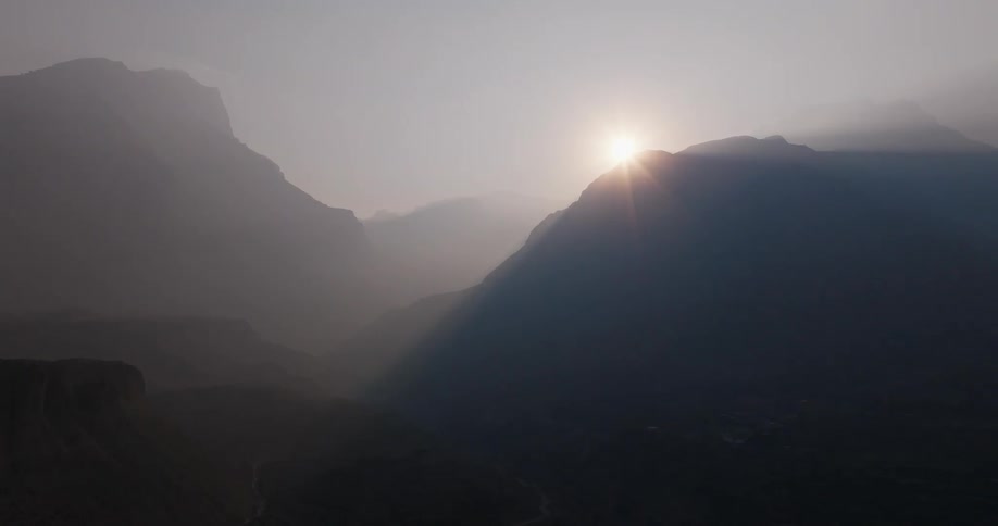 Aerial panorama of the sun on the horizon illuminating the silhouette of mountains