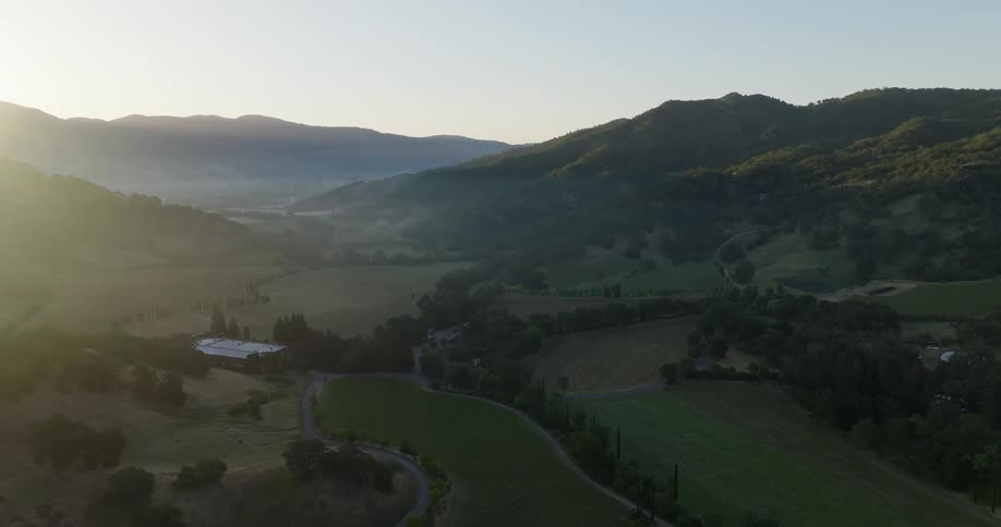 An aerial view of a region with hills and several flat grass fields and a few scattered trees