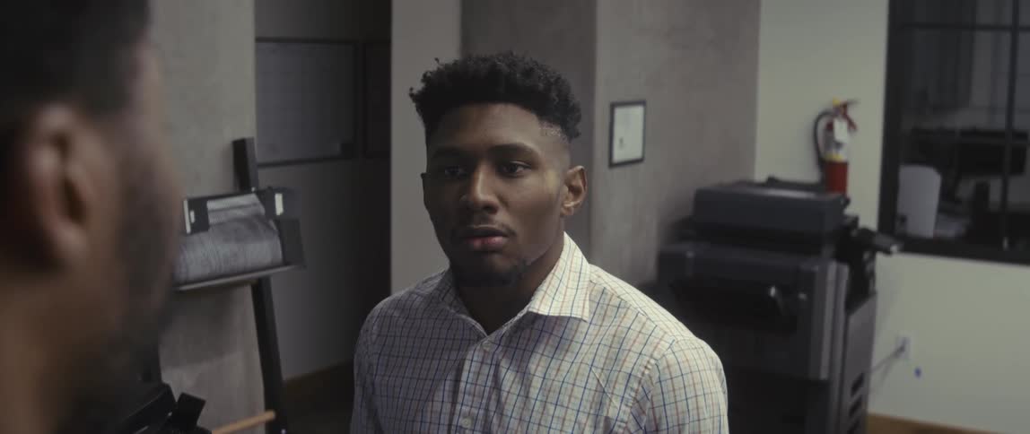 Two individuals in an office setting one wearing a plaid shirt engaged in conversation