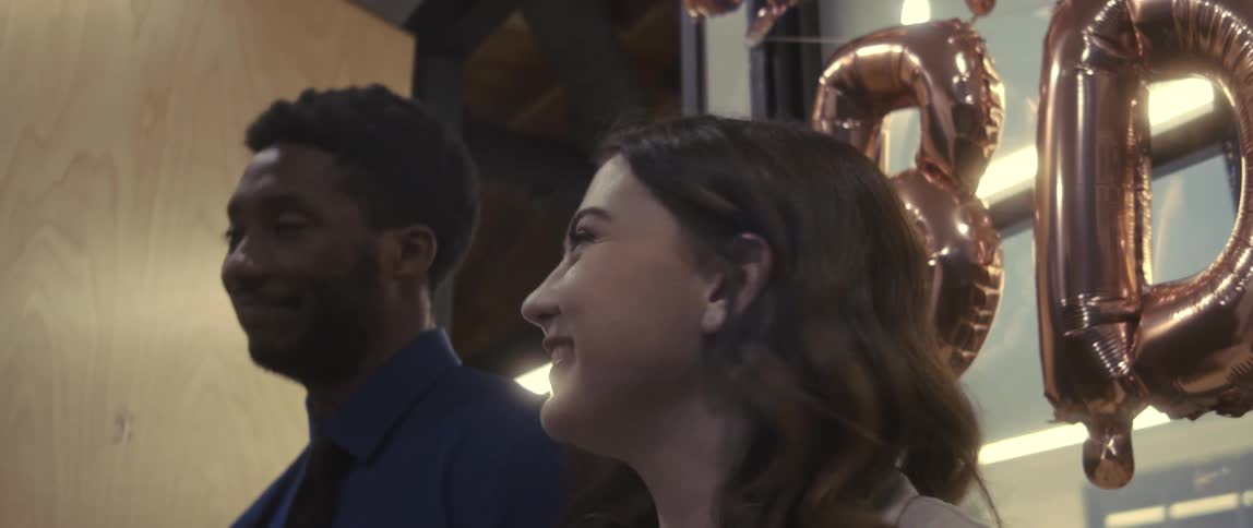 A male and female office employees laugh and talk in a room