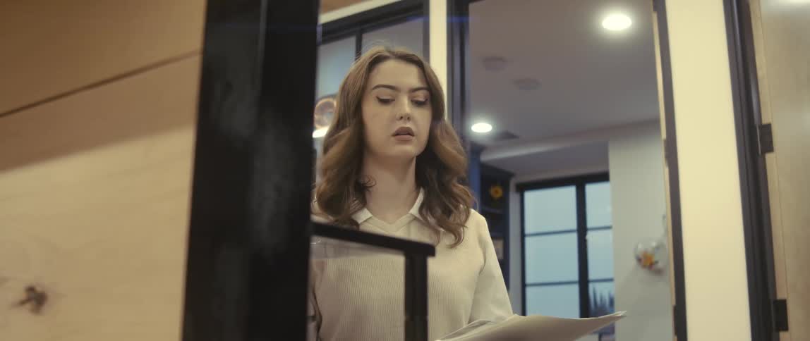 A young woman in an office makes copies of papers in folders when a man in a suit drops off another folder to which she nods and smiles before he leaves