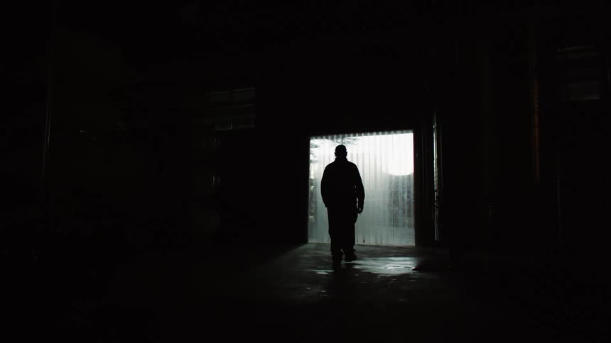 Silhouette of a man walking towards a lit door