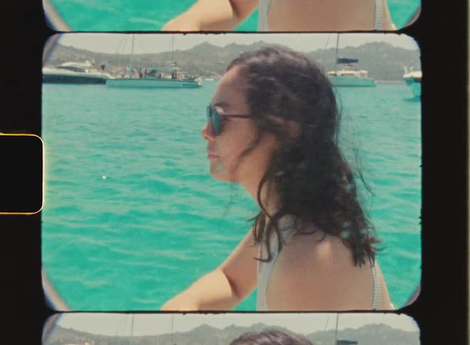 Super 8 film of a woman in a boat on the ocean who smiles and looks at several boats bobbing in the water