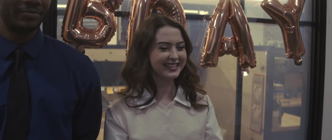 Cheerful man and woman standing side by side at a birthday celebration in a work environment