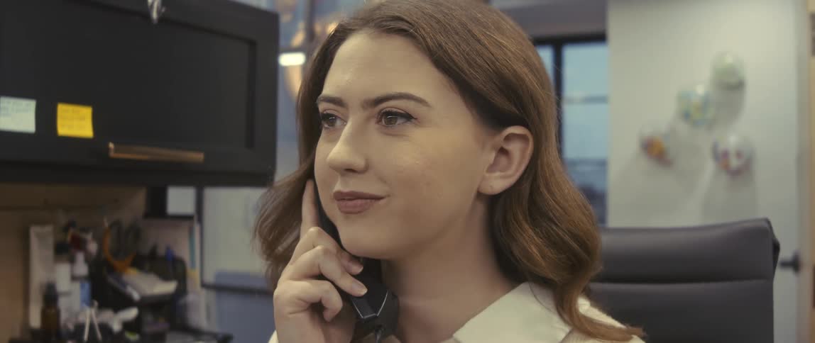A female employee in an office cubicle smiles as she speaks on a phone