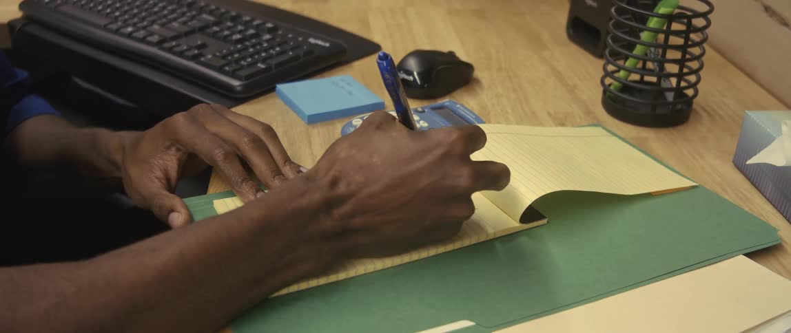A mans hands use a pen to write in a yellow legal pad