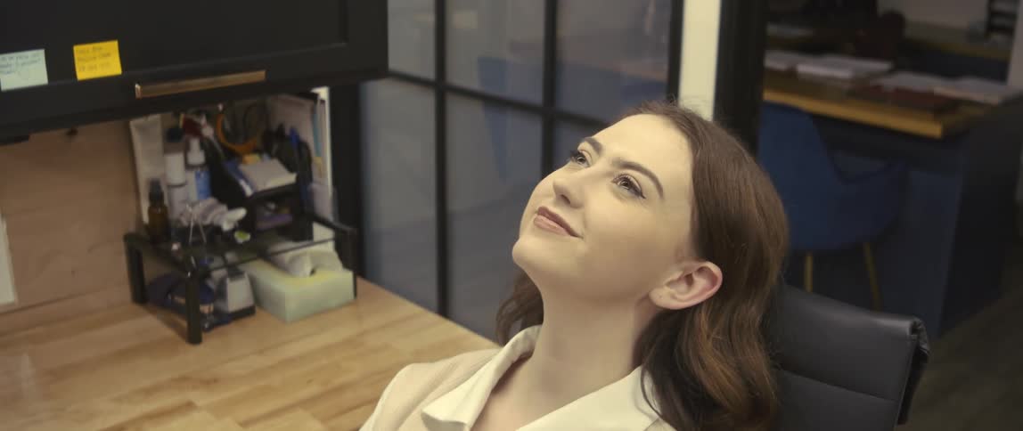 A young woman sitting in an office chair and is rocking the chair and she has a small smile of relief on her face