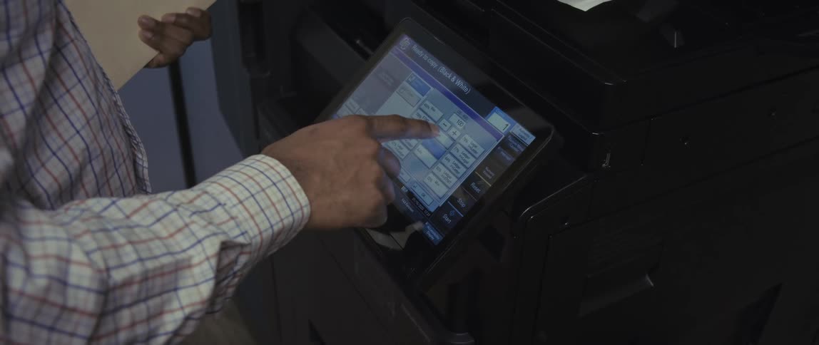 A mans hand presses buttons on a copier display screen