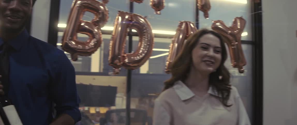 Two office workers surprise their colleague with a birthday song and presents