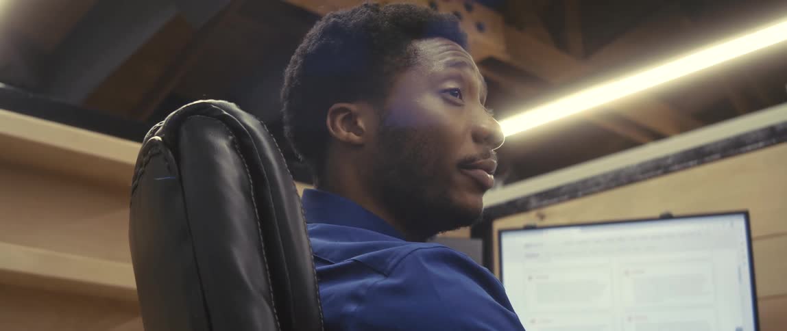 Businessman wearing a blue shirt sits in armchair talking to his coworkers at the office