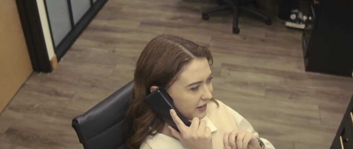 Man and a woman sitting at an office desk both talking on a phone