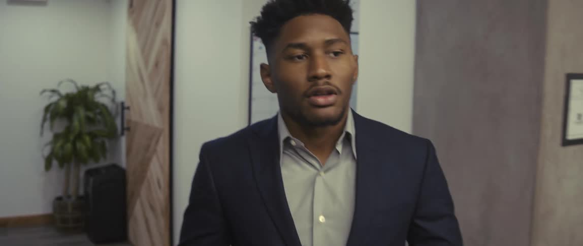 A young man in business attire is walking in an office while he is looking at documents in his hand