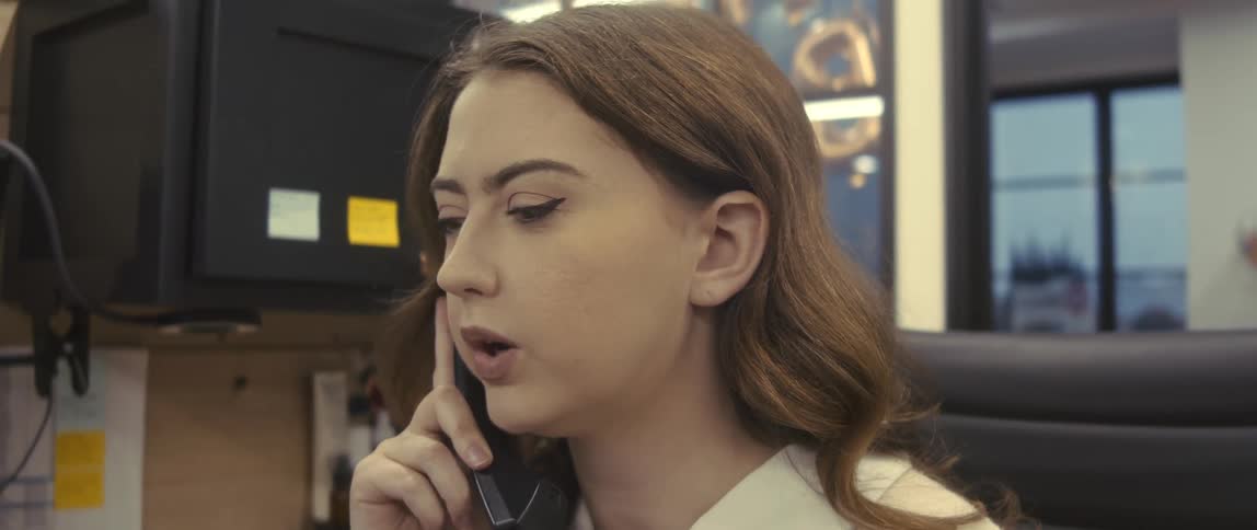 An office worker wearing a white shirt talking on the phone in her cubicle
