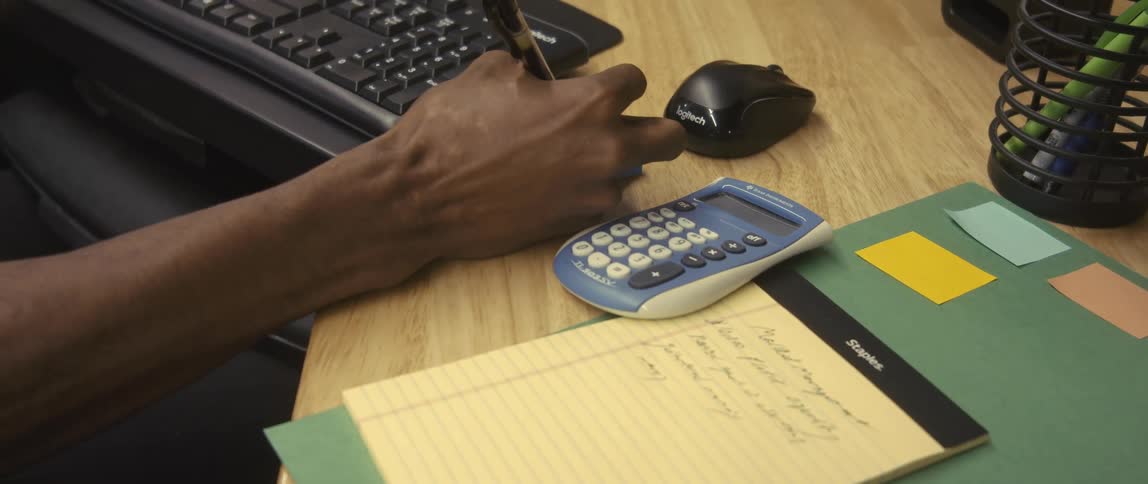 A male employee sits in a cubicle writing on a pad of sticky notes
